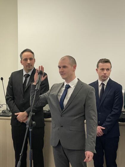 Trois hommes en costumes dans une grande salle pour une prestation de serment